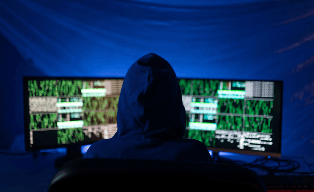 hooded figure from behind, looking at computer screens with code