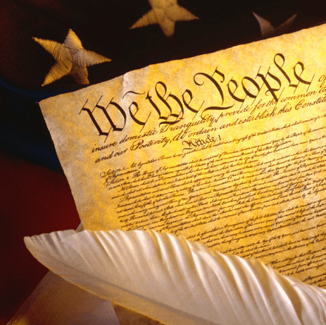 feather quil laying on the US constitution laying on a US flag